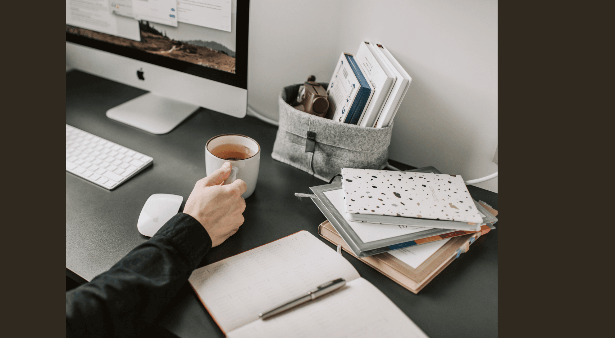 Hand holding a fresh mug of coffee at a workspace